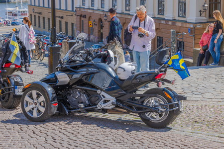 View of elderly tourist capturing moment with his camera, photographing unique motorcycle adorned with national Swedish flag. Sweden. Stockholm.のeditorial素材