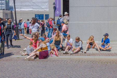 View of people sitting on sidewalk, eagerly awaiting parade in celebration of Sweden's National Day....