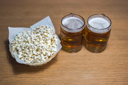 Close-up view of two beer mugs with frothy beer and popcorn cup isolated on background.の写真素材