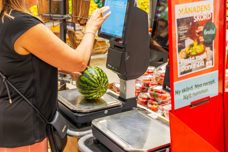 Close-up view of a woman weighing a watermelon at a self-checkout kiosk in a grocery store.のeditorial素材