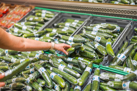 Close-up view of a hand picking up a cucumber wrapped in vacuum packaging from the shelf in the store.のeditorial素材