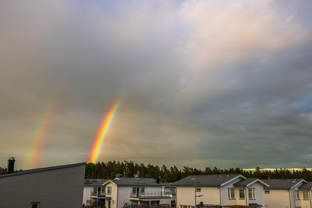 Beautiful view of double rainbow in sky with clouds after rain, over villa community and pine trees.の写真素材