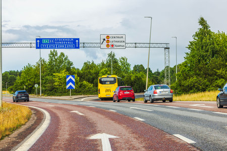 Highway junction with overhead road signs, cars and bus driving on clear day.