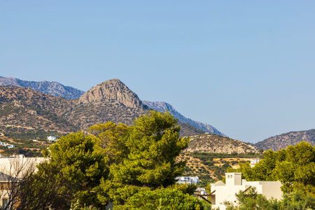 Mountain landscape with green trees and white buildings in foreground under clear blue sky. Crete.の写真素材