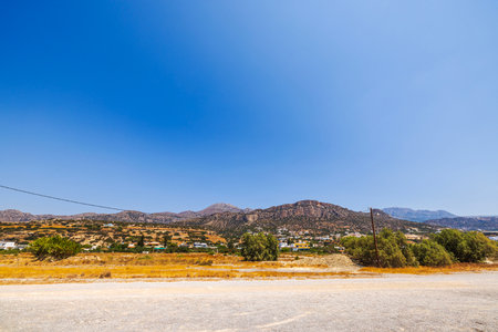 Beautiful view of coastal mountain landscape along Mediterranean Sea, with gravel road and villas nestled at base of mountains on Crete.の写真素材