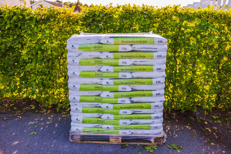 Close up view of palette with bags of soil for lawn restoration on parking spot next to garden hedge.のeditorial素材