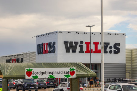 Exterior of Willys supermarket with Strawberry Paradise market stall and parked cars under cloudy...
