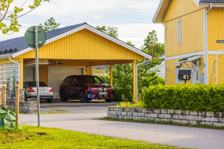 Close-up of villa with yellow-painted wooden house and garage, featuring BMW iX40 electric car and Mercedes inside the garage.のeditorial素材