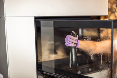 Close-up view of womanâs hand spraying cleaner on glass fireplace door to remove soot and grime.の写真素材