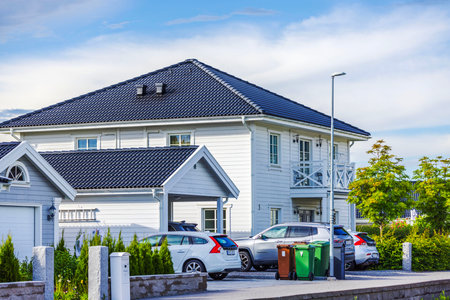 Modern white suburban house with tiled roof, parked cars, and green landscaping on sunny day.のeditorial素材