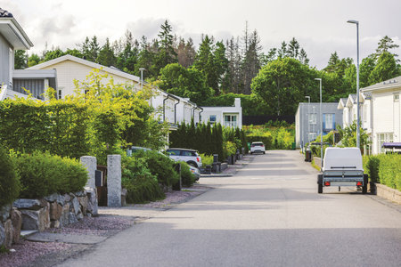 Quiet suburban street lined with modern houses, green hedges, and parked cars on cloudy day.の写真素材