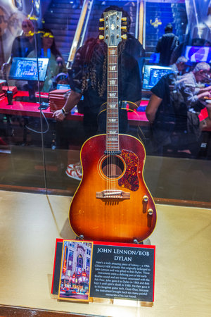 Exhibit of a Gibson J-160E guitar gifted by John Lennon to Bob Dylan, displayed in a glass case with descriptive plaque at a museum. New York. USA.のeditorial素材