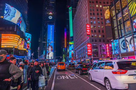 Times Square at night with pedestrians and heavy traffic under the bright lights of billboards in...