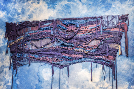 Detailed view of woven textile art hanging on blue textured wall.