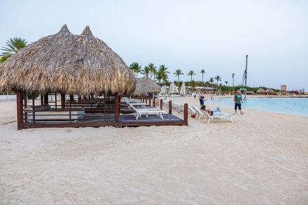 Thatched beach huts and lounge chairs on sandy beach, with people relaxing on Caribbean sea.のeditorial素材