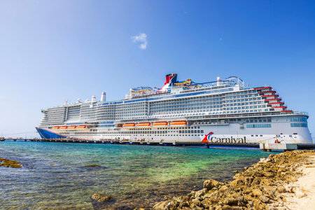Large Carnival cruise ship docked at pier in Caribbean sea with clear turquoise water and rocky shoreline.のeditorial素材