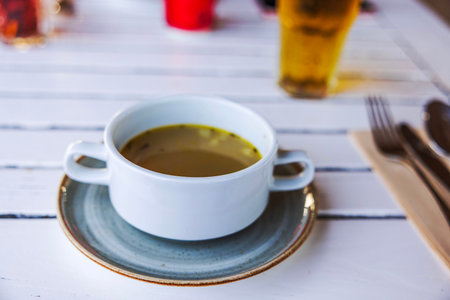 Bowl of soup on plate with utensils on white wooden table in restaurant setting. Curacao.の写真素材