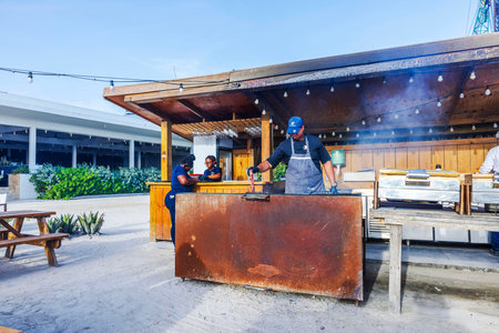 Chef preparing barbecue ribs in an open-air restaurant kitchen with large grill.のeditorial素材