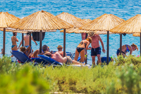 People relaxing on sunbeds under straw umbrellas by Mediterranean sea on sunny beach. Crete. Greece.のeditorial素材
