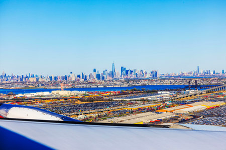 Aerial view of New York City skyline, Hudson River, and industrial shipping area with airplane wing in foreground.の写真素材