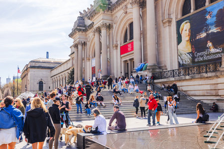 Visitors gather on The Met steps, enjoying the sunny day outside the iconic museum, surrounded by art banners and columns. New York. USA.のeditorial素材