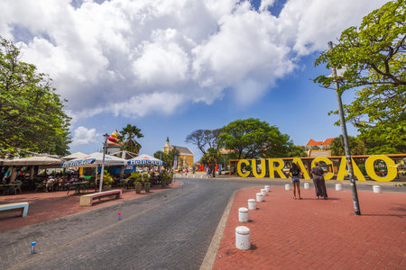 Cafe with Heineken sign near large yellow Curacao letters on an open square under cloudy sky. Willemstad. Curacao.のeditorial素材