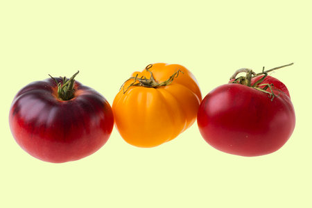 Close-up view of heirloom tomatoes in red, purple, and yellow varieties, isolated on pale yellow background.の写真素材