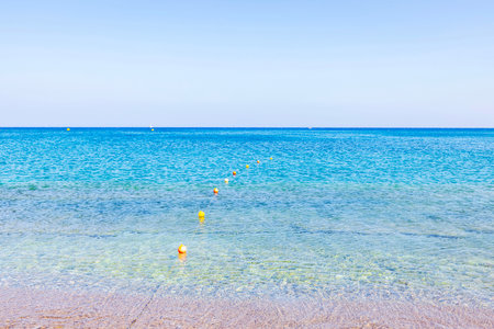 Transparent turquoise water of Aegean Sea with safety buoys sandy beach and clear skies. Rhodes. Greece.の写真素材