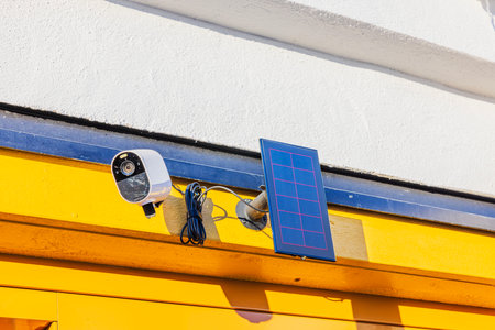 Outdoor security camera mounted on yellow wall with solar panel, capturing sunlight for eco-friendly surveillance. Sweden.の写真素材