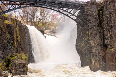 Powerful waterfall cascading between rocky cliffs with an iron bridge overhead in Paterson, New Jersey. USA.の写真素材