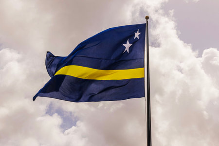 Curacao flag waving on flagpole against cloudy sky on breezy day.の写真素材