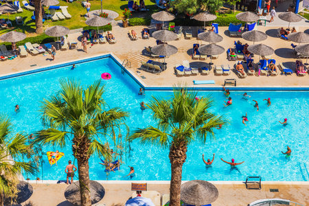 Aerial view of outdoor pool hotel surrounded by palm trees, sunbeds, umbrellas and people. Rhodes. Greece.の写真素材
