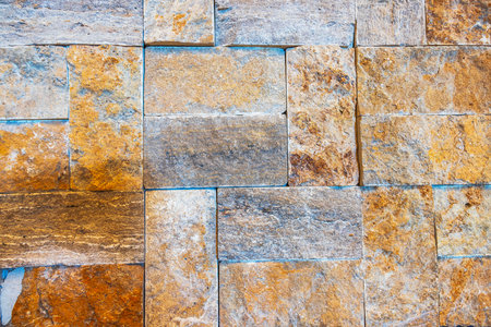 Close-up of textured stone wall with natural orange and brown tones showing unique patterns and rugged surfaces.の写真素材