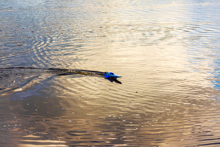 Blue remote-controlled speedboat gliding across water with rippling reflections of the sky at sunset. Sweden.の写真素材
