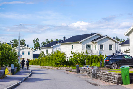 Modern residential street with white villas, green gardens, parked cars, and two boys walking under clear sky.のeditorial素材