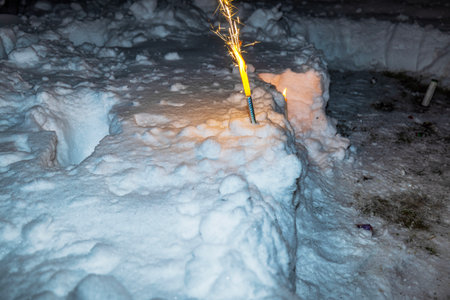 Burning sparkler standing vertically in deep snow on winter evening creates festive glow on New Year's Eve.の写真素材