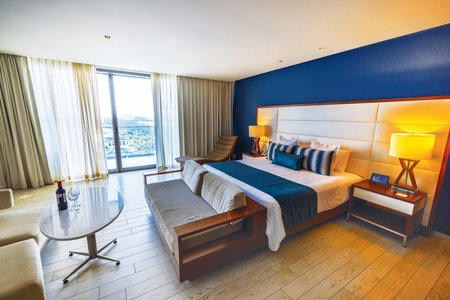 Elegant hotel room interior with large bed, cozy furniture, blue accent wall, bright natural light and city view. Cancun. Mexicoのeditorial素材