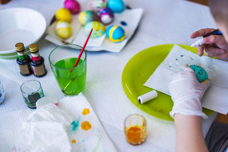 Child decorating Easter egg with creative patterns using food coloring, surrounded by colorful tools and painted eggs. Sweden.の写真素材