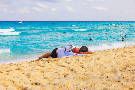 Man resting on sandy beach near Caribbean Sea under sunny sky with turquoise water and gentle waves. Cancun. Mexico.のeditorial素材