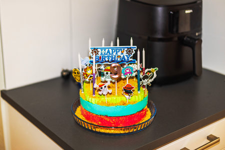 Colorful birthday cake with pirate-themed decorations, candles, and "Happy Birthday" sign, celebrating ninth birthday.のeditorial素材