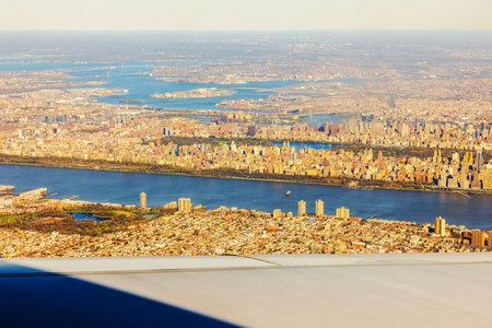 Aerial view of New York City with Hudson River and Manhattan skyline glowing in warm sunlight through airplane window.の写真素材