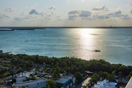 Scenic view of Caribbean Sea reflecting sunlight, with boat sailing near lush green coastline and tropical resort buildings. Cancun. Mexico.のeditorial素材