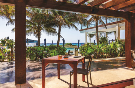 Relaxing tropical terrace view with wooden table and chair overlooking palm trees, pool and turquoise Caribbean sea. Cancun. Mexico.の写真素材