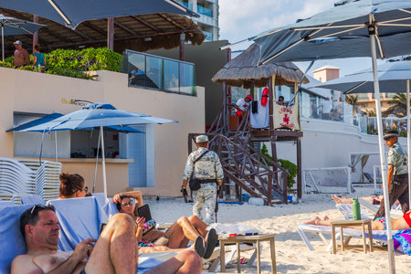 Armed military personnel patrol beach resort with lifeguard station and tourists relaxing under umbrellas on Caribbean sea. Cancun. Mexico.のeditorial素材