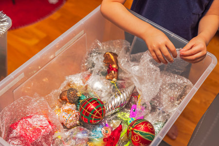 Child's hands carefully handling bubble wrap over colorful Christmas ornaments in plastic storage box. Sweden.の写真素材