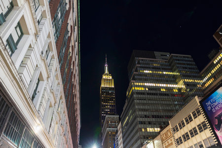 Empire State Building illuminated at night surrounded by classic and modern buildings under dark clear sky. New York. USA.のeditorial素材