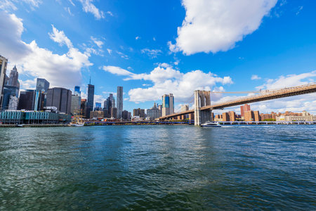Brooklyn Bridge spanning East River with New York City skyline under bright blue sky and white clouds. New York. USA.のeditorial素材