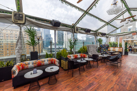 Modern rooftop lounge with panoramic city views, stylish seating, lush greenery, glass ceiling, and cozy atmosphere under cloudy sky. New York. USA.のeditorial素材