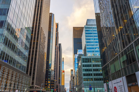 Skyscrapers towering along bustling New York City street reflecting golden sunset light against cloudy sky. New York. USA.のeditorial素材