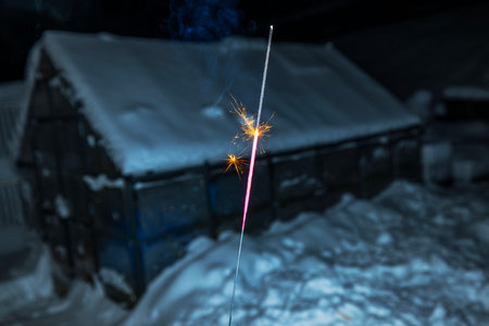 Burning sparkler illuminating snowy winter New Year night scene with building covered in snow in background. Sweden.の写真素材